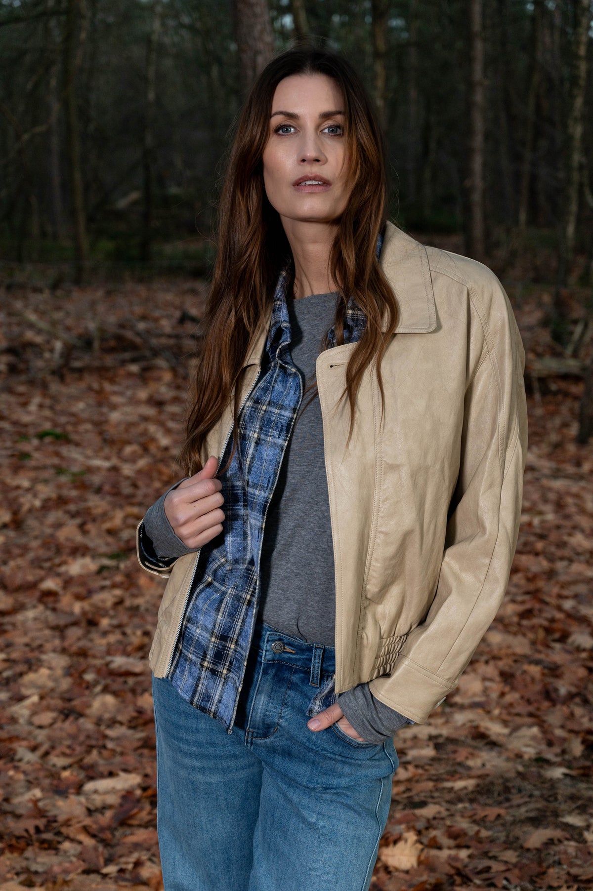 lichtbeige lederlook jas gedragen op een geruite blouse met een grijs shirt eronder