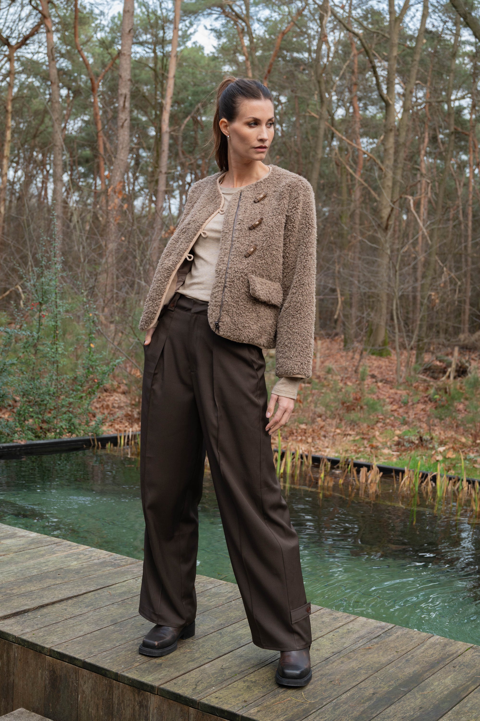 zie de details van de sevilla pantalon bruin, waarbij je onderaan de pijpen knoopdetails hebt zitten waarmee je de pijpwijdte kunt aanpassen