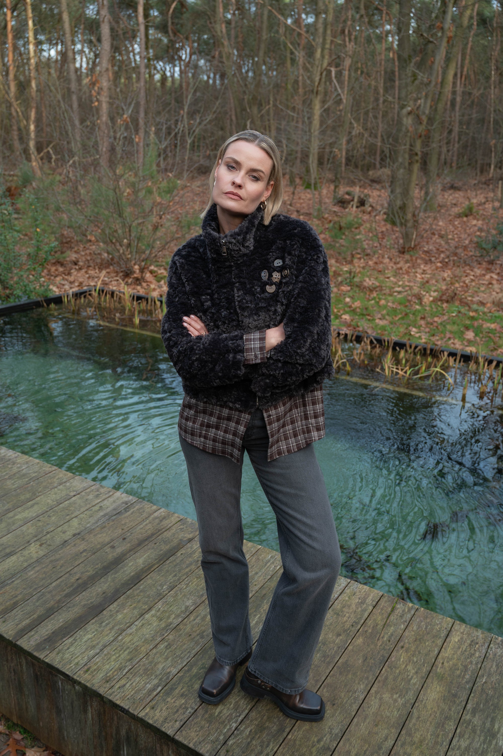 model draagt complete herfstoutfit met zwartgrijs teddyjasje, geruite bruine blouse op een spijkerbroek