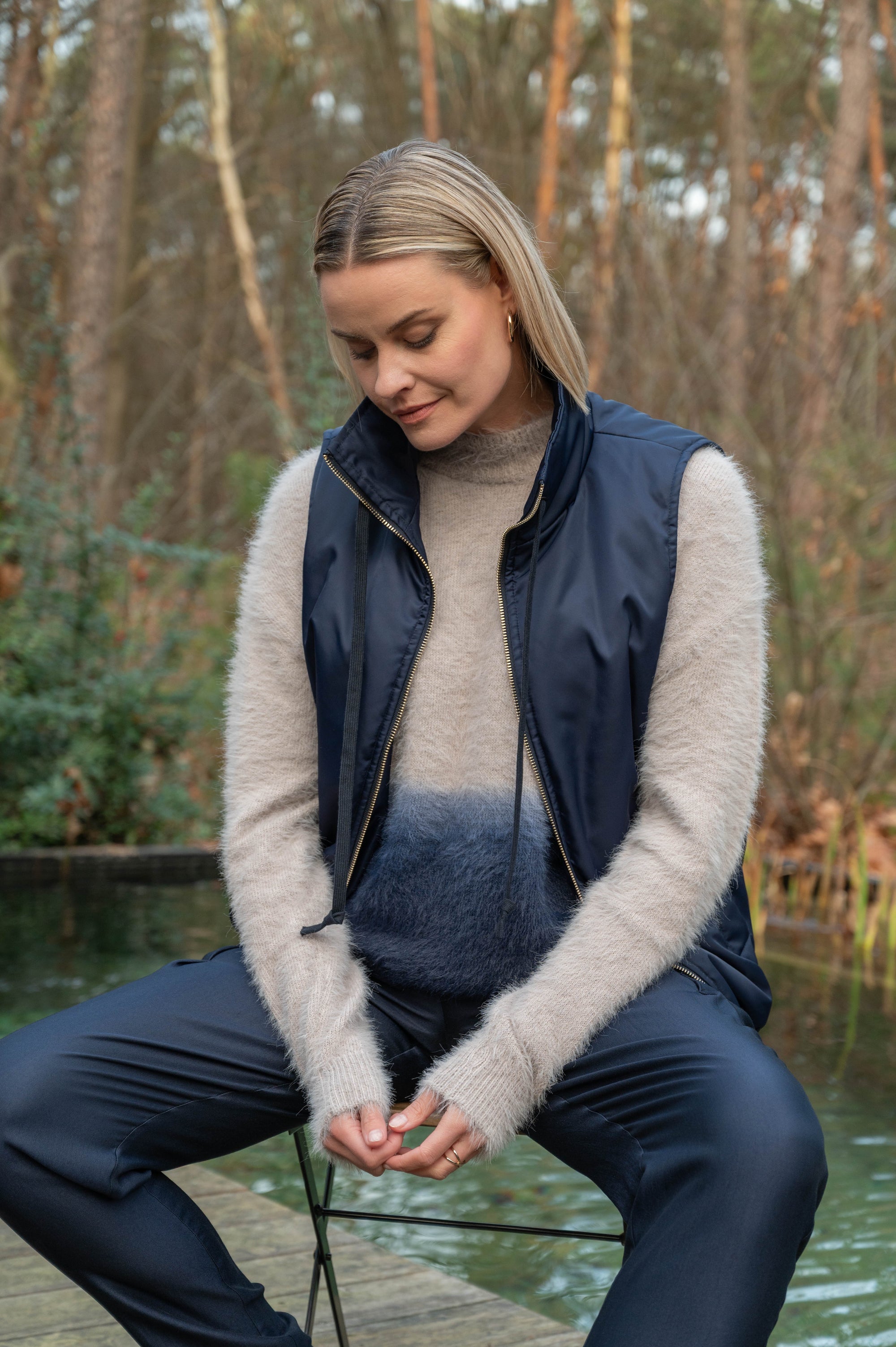 model draagt een complete outfit met een blauwe bodywarmer over een warme herfsttrui met kleurverloop