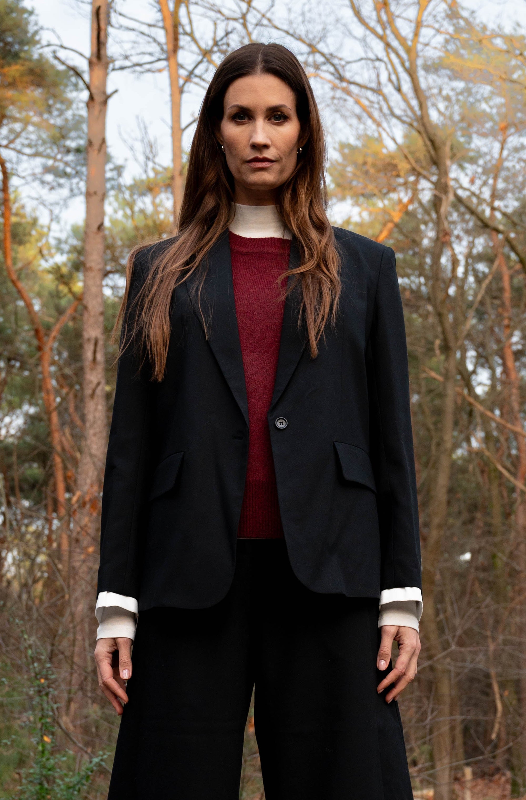 model draagt de zwarte blazer met witte manchetten aan de onderkant van de mouwen op een zwarte broek 