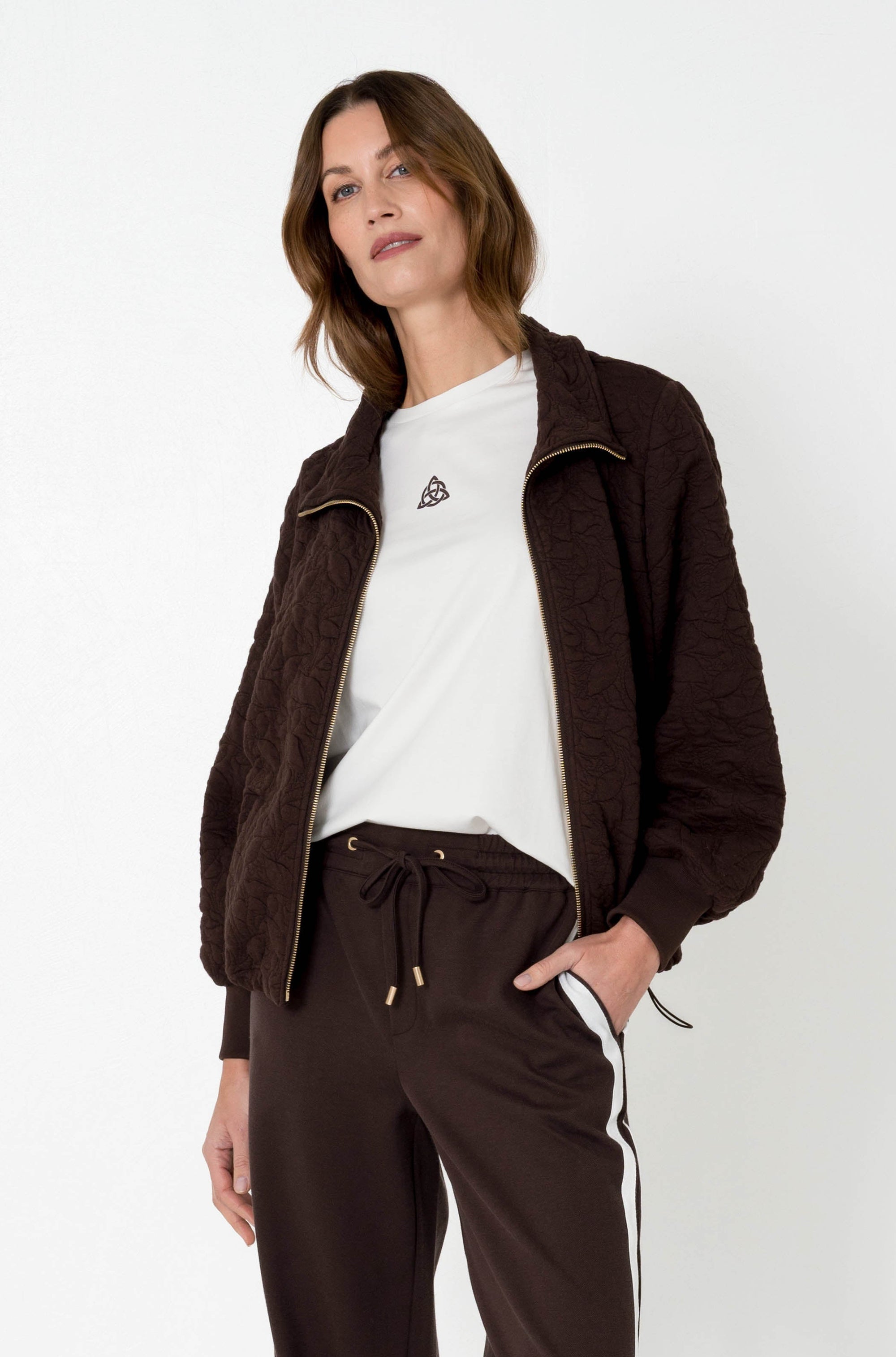 model combineert een bruin jasje vanton met een bruine broek met witte streep aan de zijkant en een wit basis shirtje onder het jasje