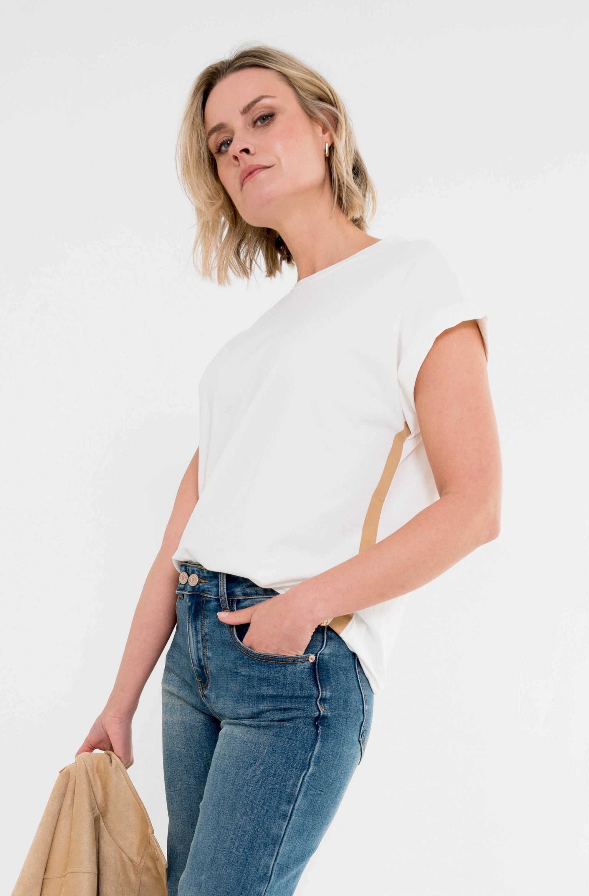 model draagt het nana offwhite t-shirt met korte mouwen en een beige streep aan de zijkant op een spijkerbroek