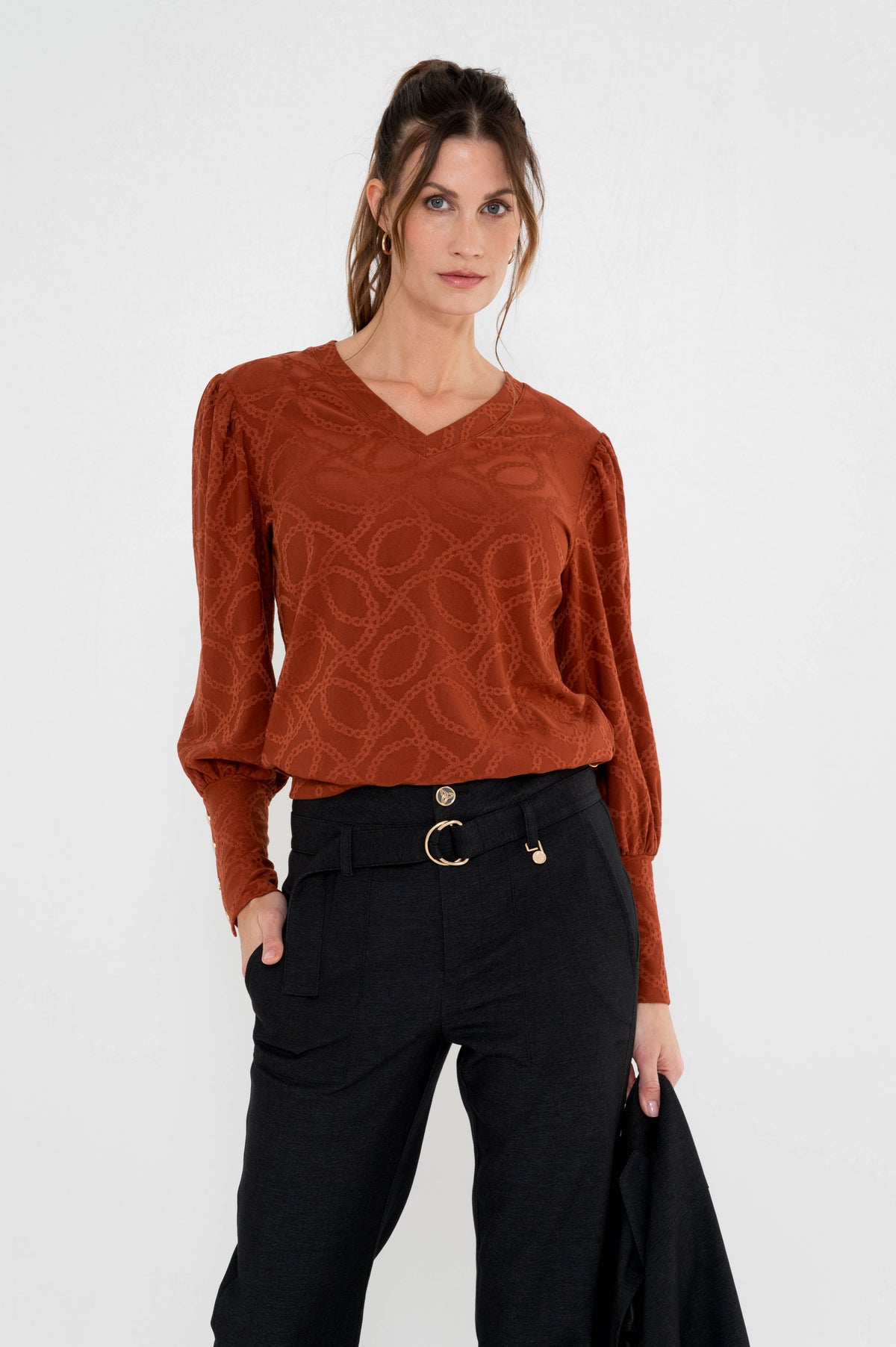 dame draagt roestbruin shirt met lange mouwen en sierlijk schakelpatroon op een zwarte nette broek 