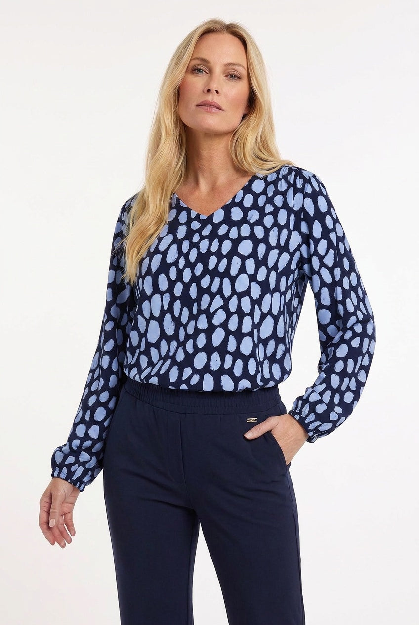 model draagt v-hals travelshirt met lange mouwen en animal dots in blauw op een donkerblauwe travelbroek