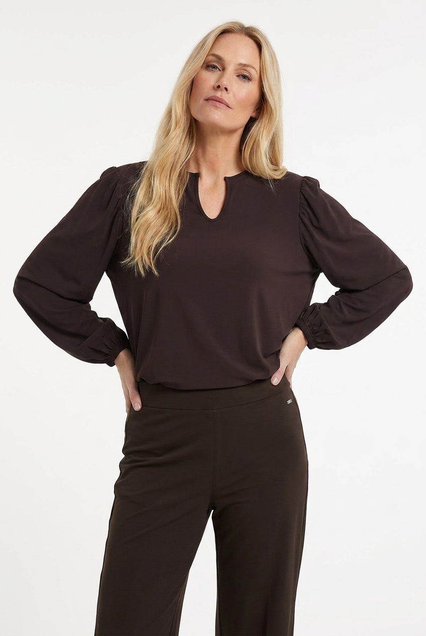 dame draagt bruin travelshirt met lange mouwen en vrouwelijke v-hals op een bruine broek