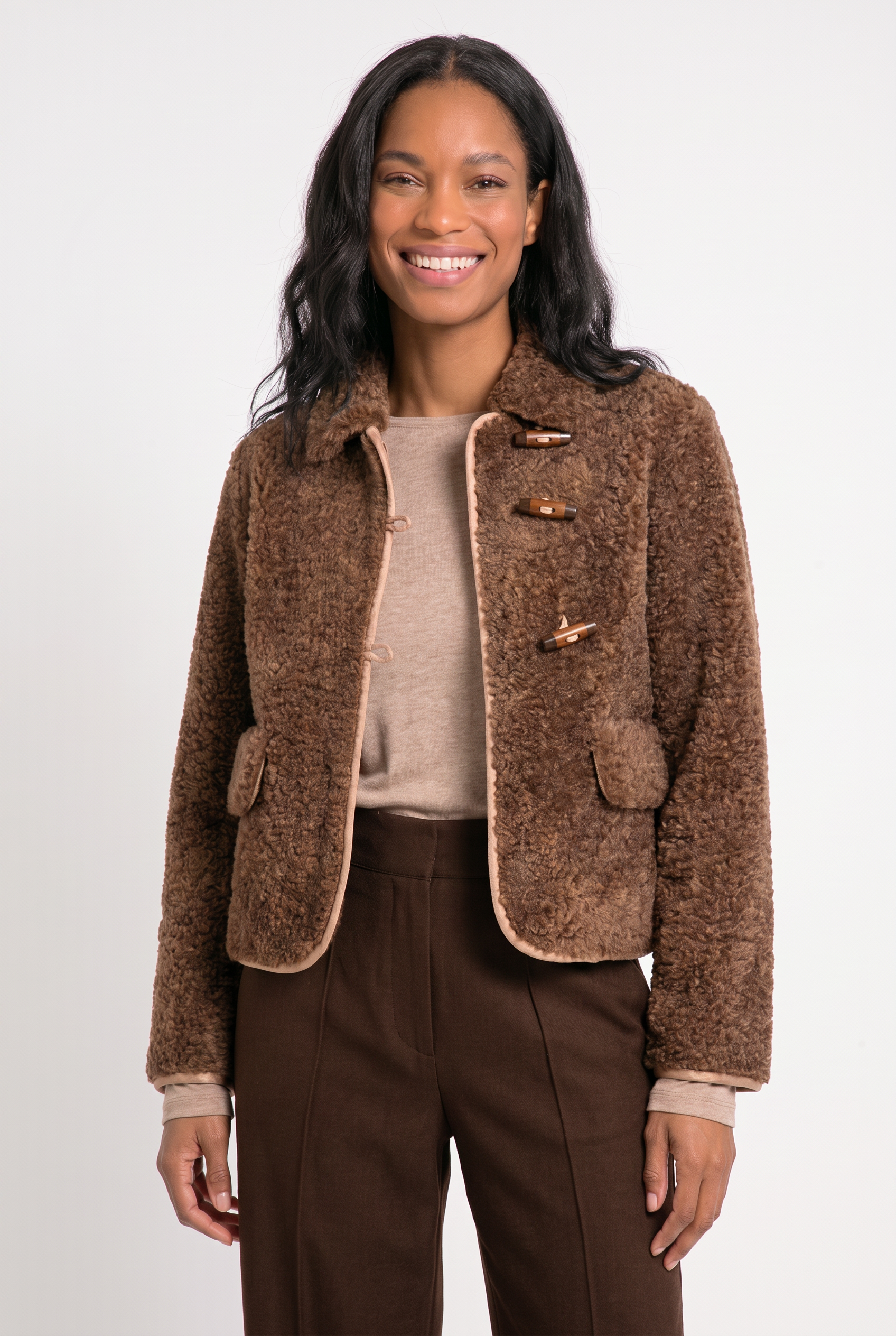 dame draagt bruin teddy jack met contrasterende bies en houtje-touwtje knopen op een bruine broek met daaronder een beige shirt met lange mouwen