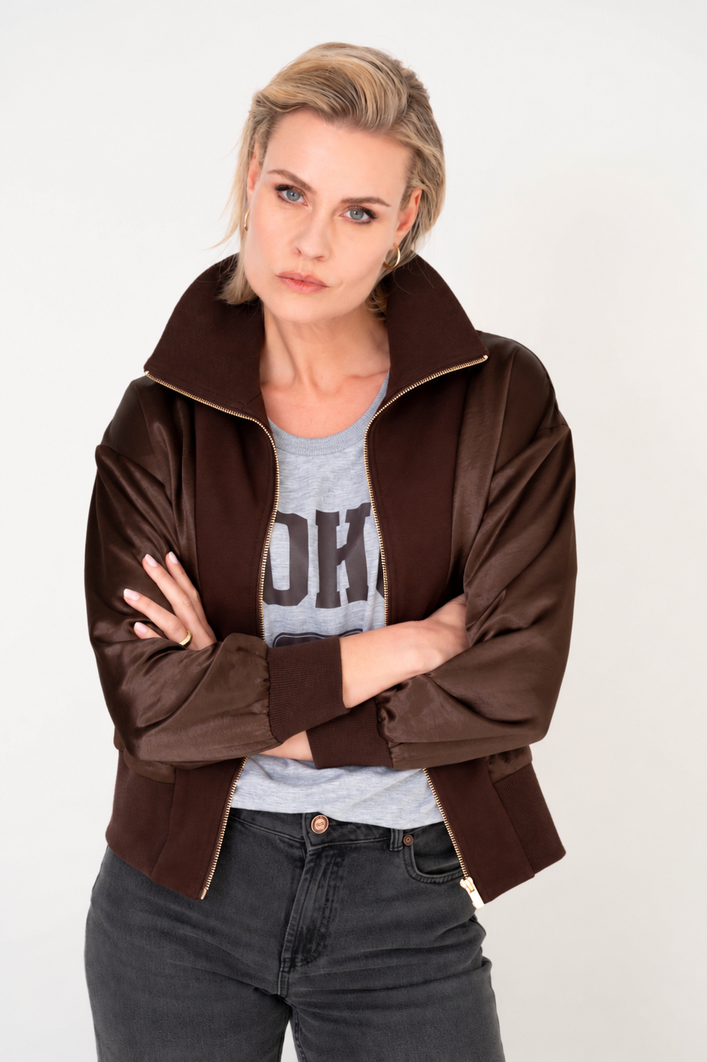 model draagt een bruin jasje op een grijze broek en met een stoer t-shirt eronder