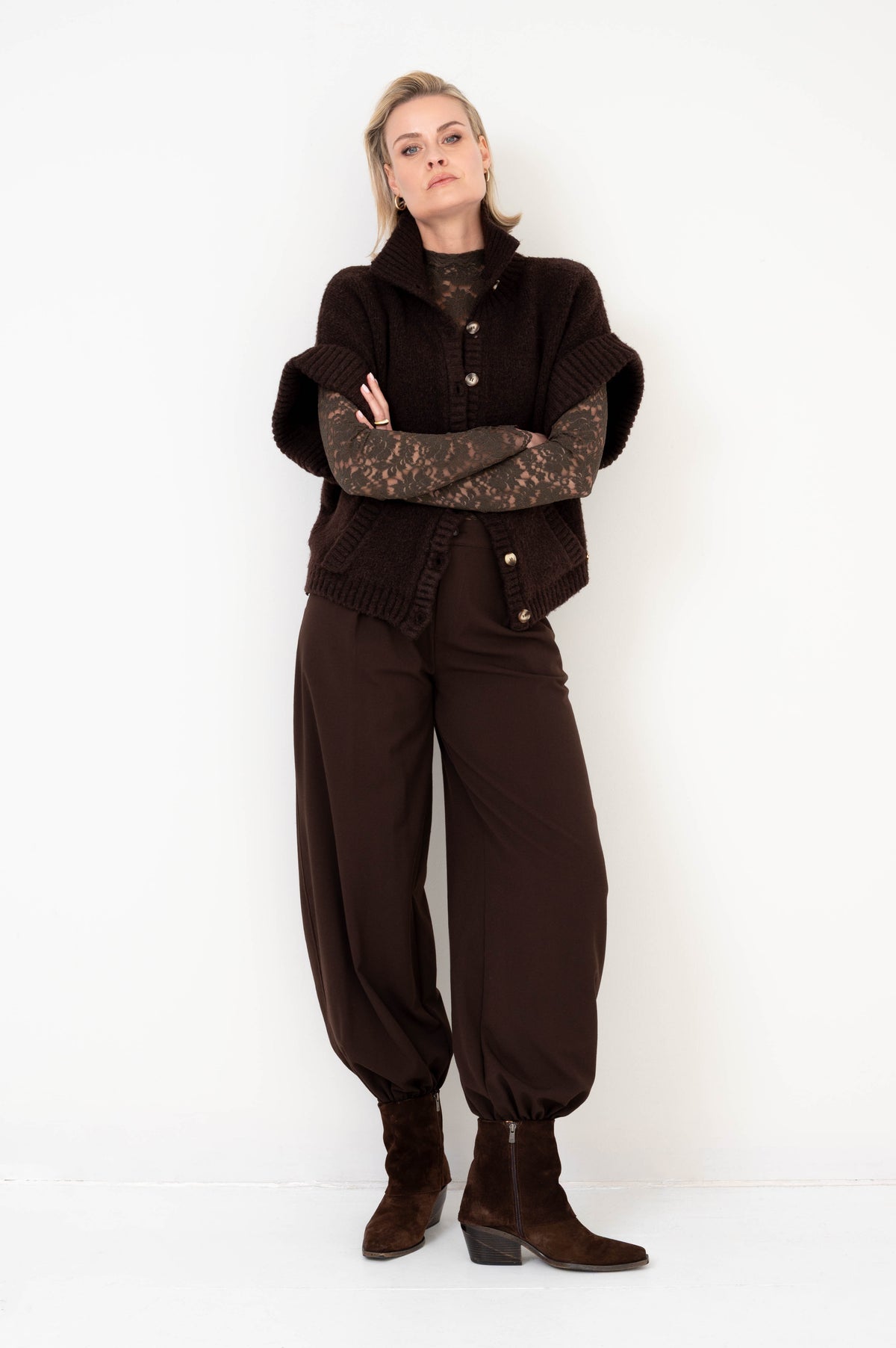 najaarsoutfit in het bruin met gebreid vest met korte mouwen en een kanten shirt met lange mouwen eronder gecombineerd op een bruine broek