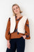 dame draagt zedan gilet op een roestbruine blouse met bloemenprint en met een donkere spijkerbroek