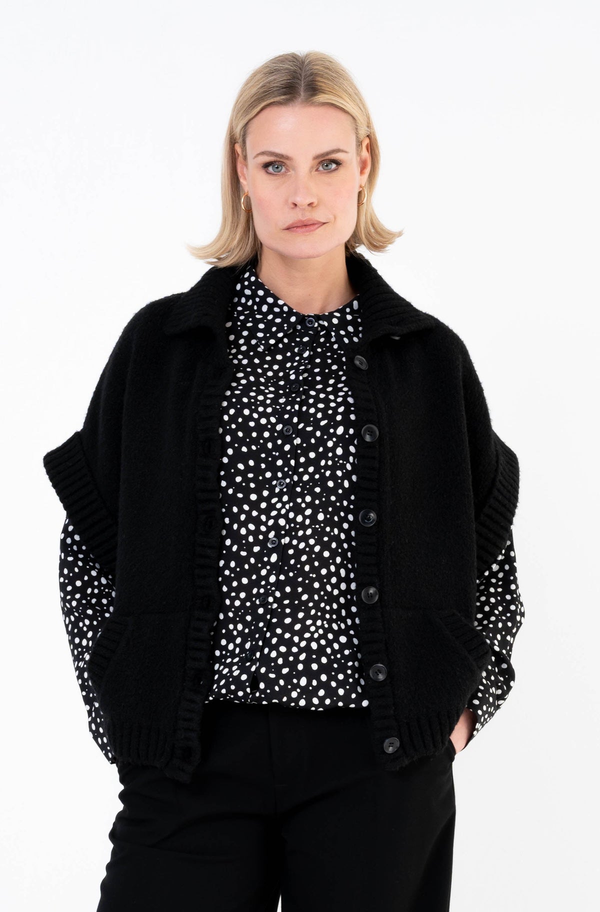 damesoutfit met zwart vest met korte mouwen op een zwarte broek gecombineerd met een blouse met zwart-wit patroon